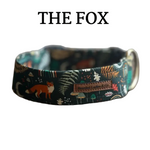 A fabric dog collar with a woodland forest pattern featuring a fox, mushrooms, ferns, and birds on a dark teal background, resting on a rustic wooden surface. The brand label reads 'Bearded Ladies Co.
