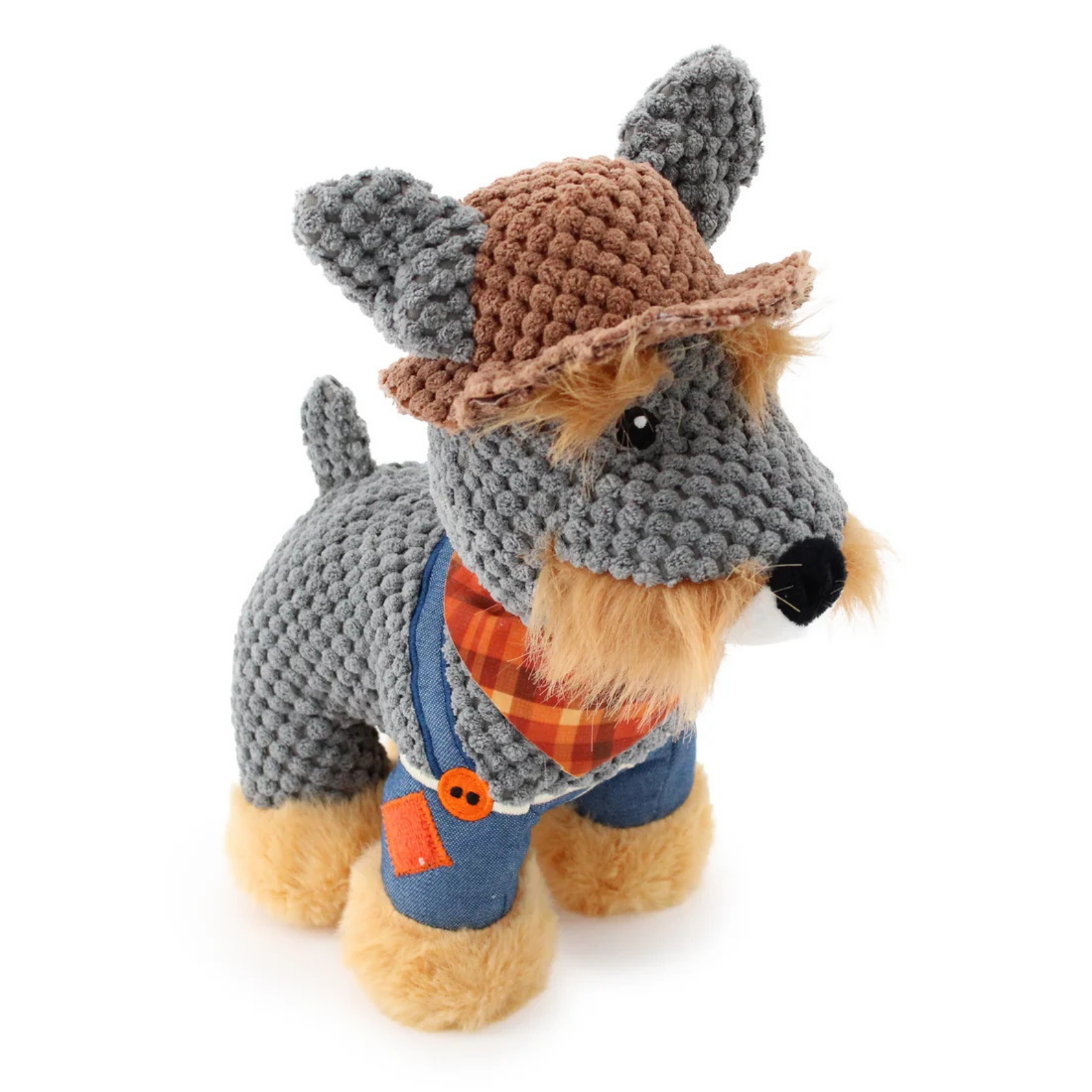 A crocheted dog toy wearing a brown hat, blue overalls, and an orange plaid bandana, photographed on a clean white background.