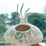 A cream, blue, and green felt pet cave with decorative strings on the top.