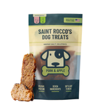 A bag of Saint Rocco's Dog Treats Pork & Apple flavor stands on a white background with two dog treats displayed in front. The packaging is dark teal and cream with a dog logo, and the treats are brown with visible chunks.