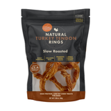 A bag of Natural Turkey Rings Slow Roasted dog chew treats, 4 count, in a dark charcoal pouch with a clear window showing the twisted ring-shaped treats inside.