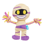 A plush dog toy shaped like a smiling mummy, with beige and purple wrap-style fabric, yellow eyes, a black mouth area, and braided rope arms in yellow and purple. A small blue tag on the side reads BARKS.