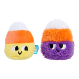 Two small plush candy corn toys on a plain white background. One is a soft yellow plush with an orange band and white tip, and the other is a fuzzy purple plush with an orange band and white tip.
