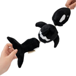 A black and white plush orca toy being held by two hands against a plain white background.