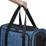 A blue pet carrier duffel bag with black handles and black mesh ventilation panels, shown with a person's hand holding the top handle against a white background.