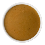 A top-down view of a thick, smooth, golden-brown puree or sauce in a white ceramic bowl against a solid white background.