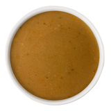 A top-down view of a thick, smooth, golden-brown puree or sauce in a white ceramic bowl against a solid white background.