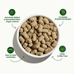 A top-down view of a white bowl filled with tan kibble pet food on a light gray background, surrounded by four green circular callout icons with text describing product qualities: humanely raised meat and organ, complete and balanced recipe, easy to feed small bites, and grain and filler free.