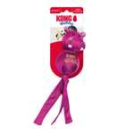 Kong Wubba dog toy in pink, featuring a hippo-shaped plush head with white teeth and a long pink ribbon tail, attached to a red and white cardboard backing card with the KONG brand logo.