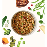 A top-down view of a round bowl filled with a textured, chunky brown and green savory mixture, surrounded by illustrated vegetables and a grilled steak on a white background.