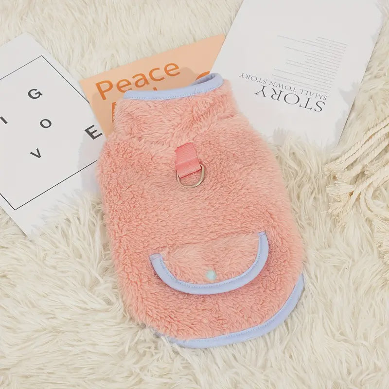 Pink fleece dog sweater on a fluffy white surface with books underneath