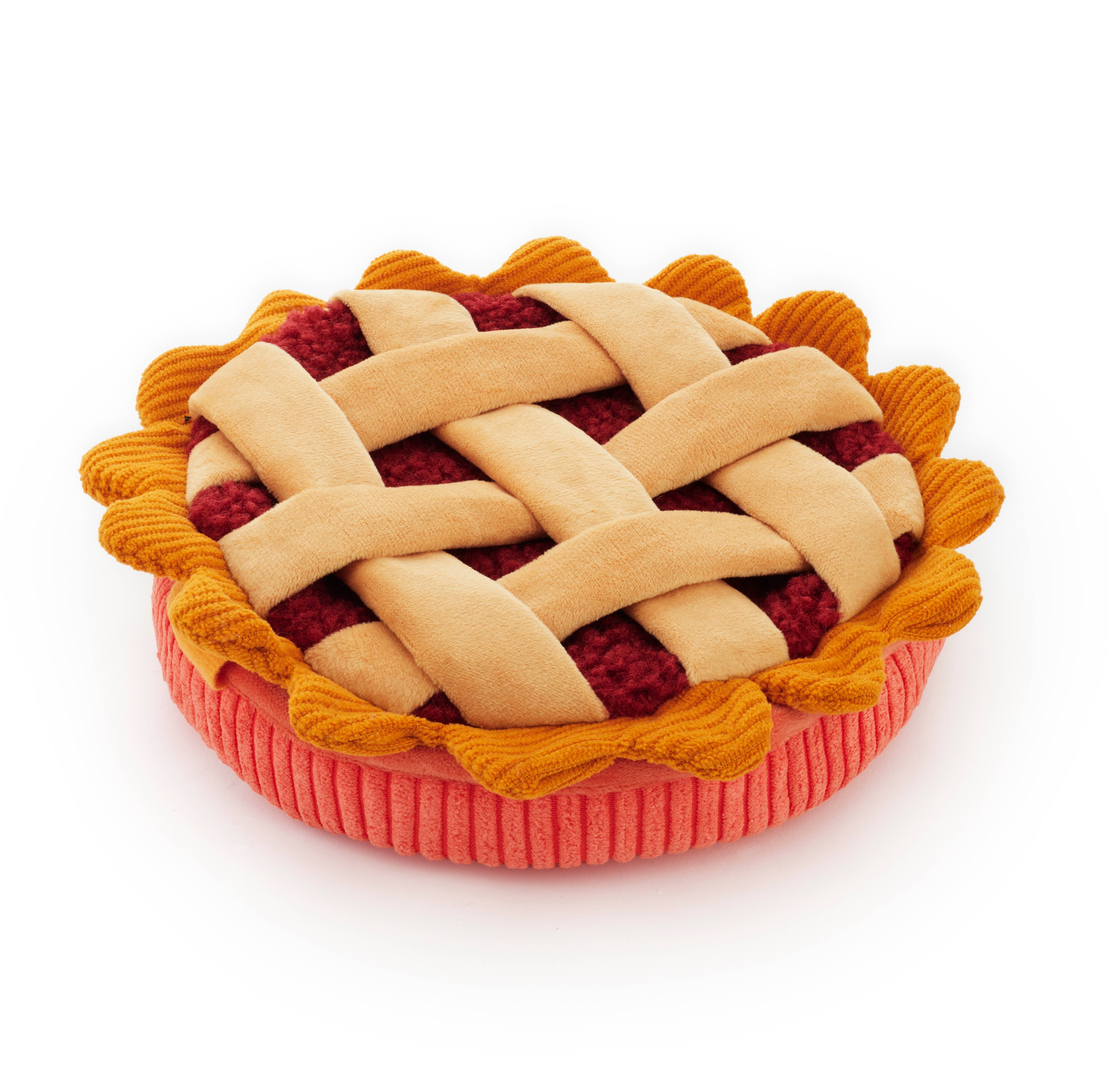 A plush dog toy shaped like a pie, featuring a beige woven lattice top, red fruit filling, and a pink crust, isolated on a white background.