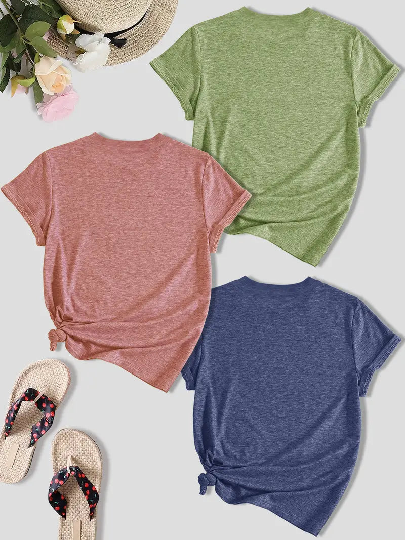 Three t-shirts in pink, green, and blue on a light surface with flip-flops and flowers.