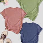Three t-shirts in pink, green, and blue on a light surface with flip-flops and flowers.