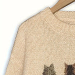 Beige sweater with cat pattern on a hanger against a white background