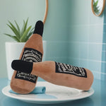 Plush toy shaped like a bottle with 'Jack Daniel's' branding on a white plate against a light blue tiled wall.