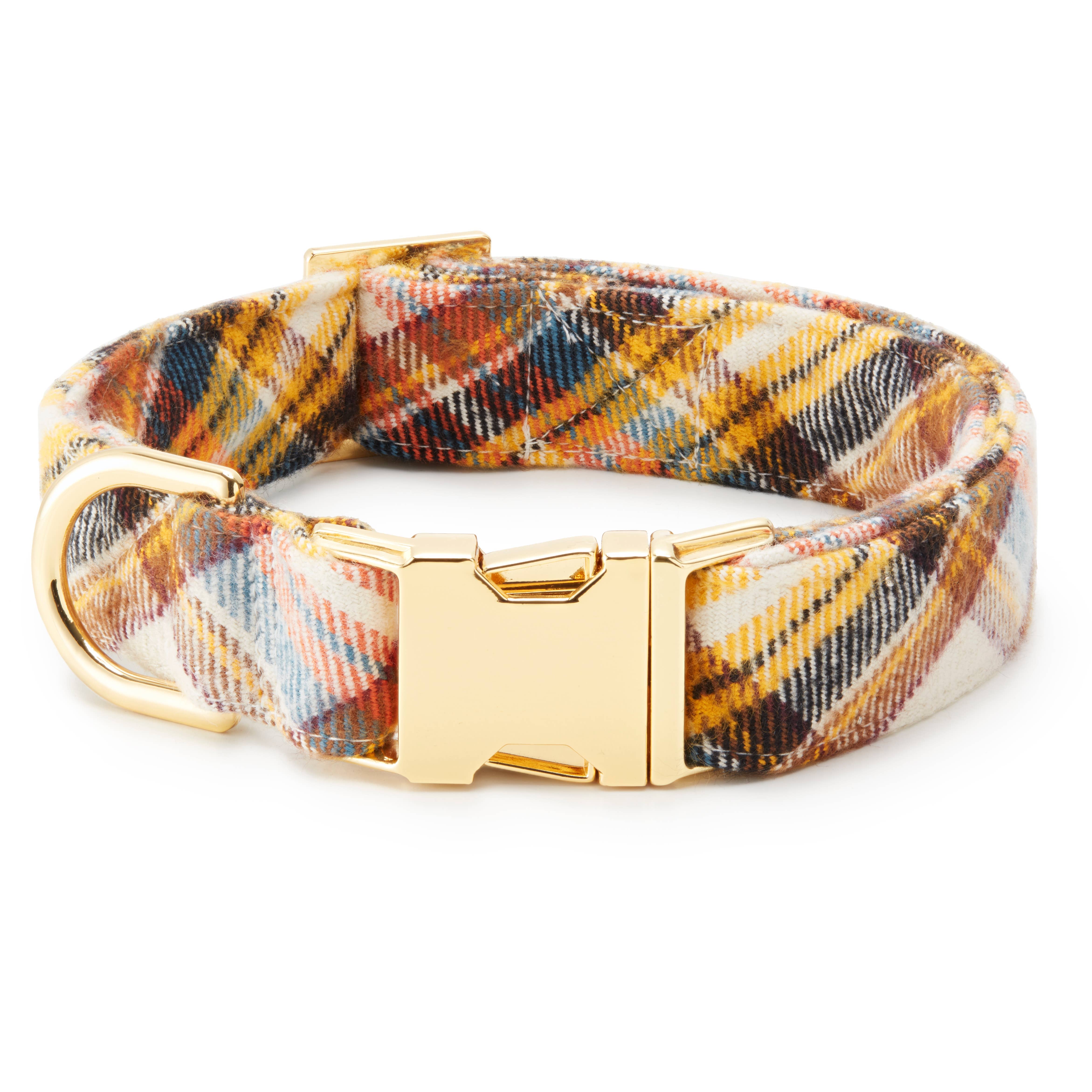A plaid dog collar with a multicolor pattern of yellow, blue, brown, and white, featuring a gold-tone metal buckle and D-ring, shown on a white background.