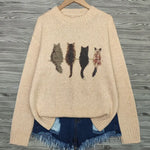 Beige sweater with cat illustrations on a wooden hanger against a wooden background
