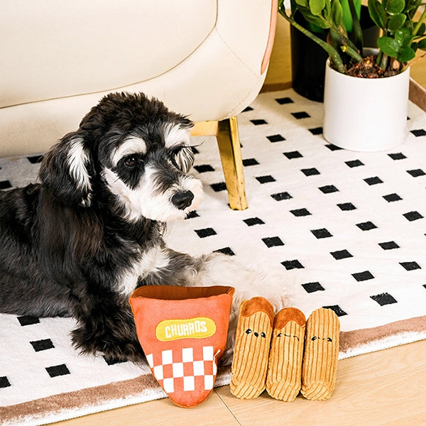 Dog playing with a Churros-shaped toy on a checkered rug