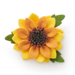 A felt flower brooch shaped like a sunflower, featuring yellow and orange petals, a dark brown center, and green leaves, shown on a plain white background.