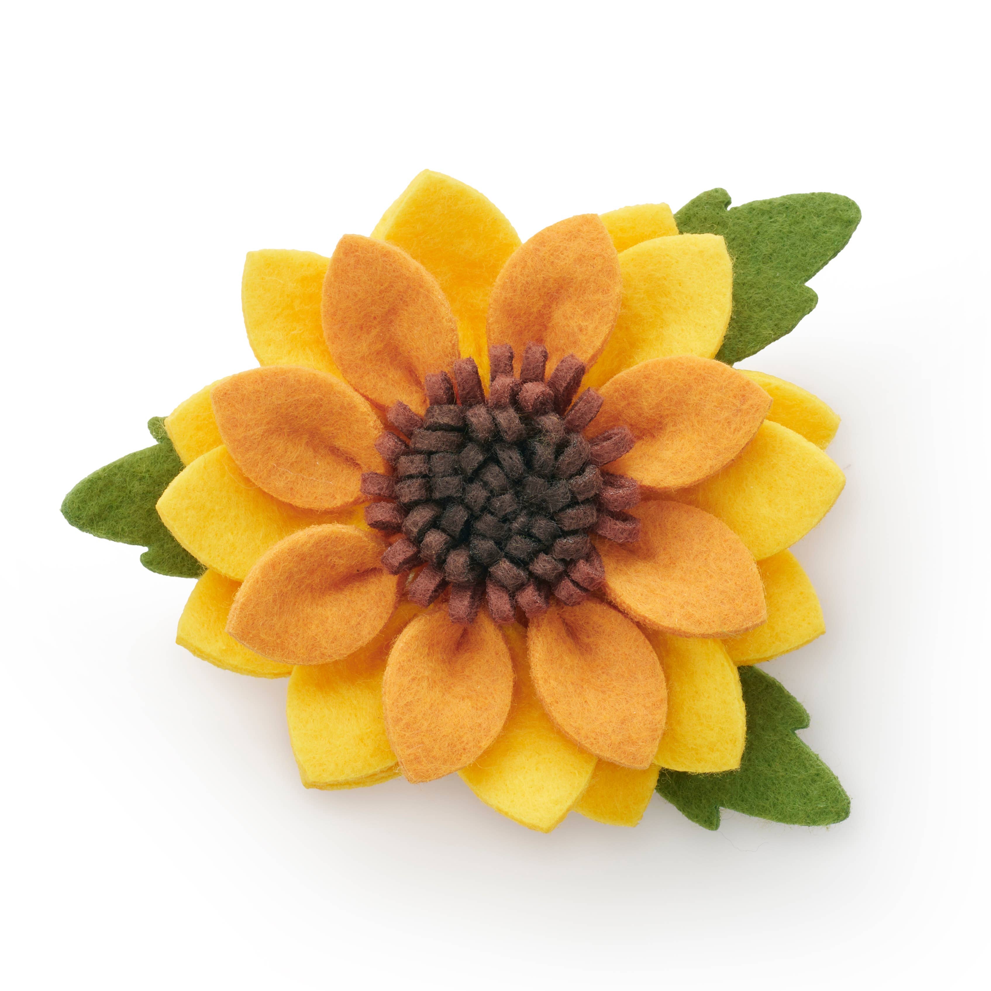 A felt flower brooch shaped like a sunflower, featuring yellow and orange petals, a dark brown center, and green leaves, shown on a plain white background.