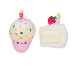Two plush toy desserts on a plain white background: a cupcake plush with pink frosting base, multicolored sprinkles, a yellow candle, and a smiling face, next to a slice-of-cake plush with cream layers, a strawberry topper, and a candle.