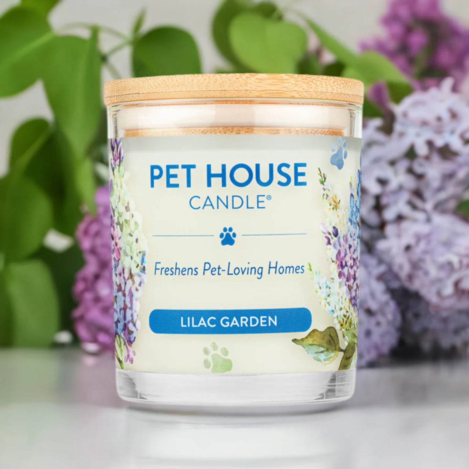 Pet House Candle labeled 'Lilac Garden' with a floral design on a blurred background of green and purple flowers.