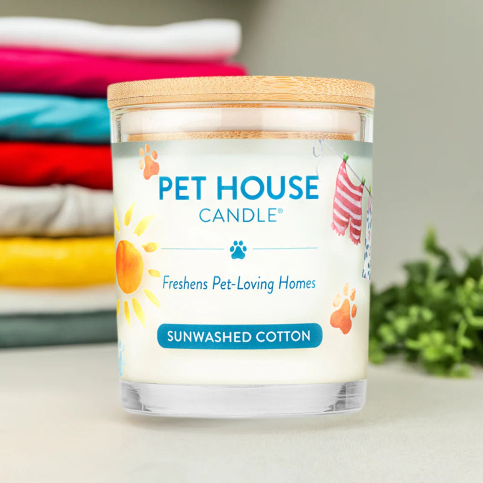 Pet House Candle labeled 'Sunwashed Cotton' with a stack of folded clothes in the background.