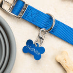 Blue dog collar with a bone-shaped tag labeled 'MidNite' on a beige surface with a bone and bowl.