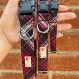 Three plaid dog collars held in a hand against a brick wall background