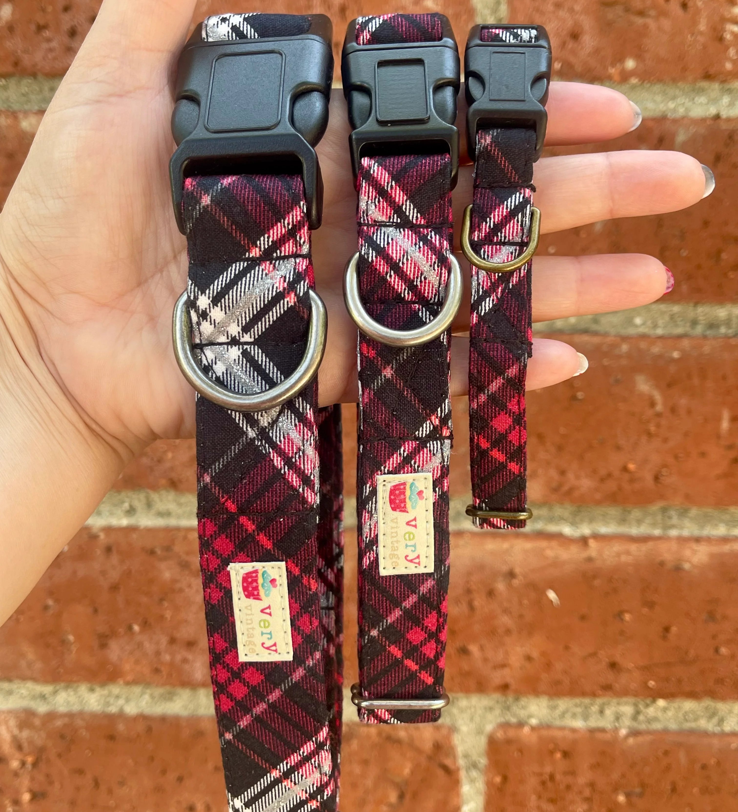 Three plaid dog collars held in a hand against a brick wall background