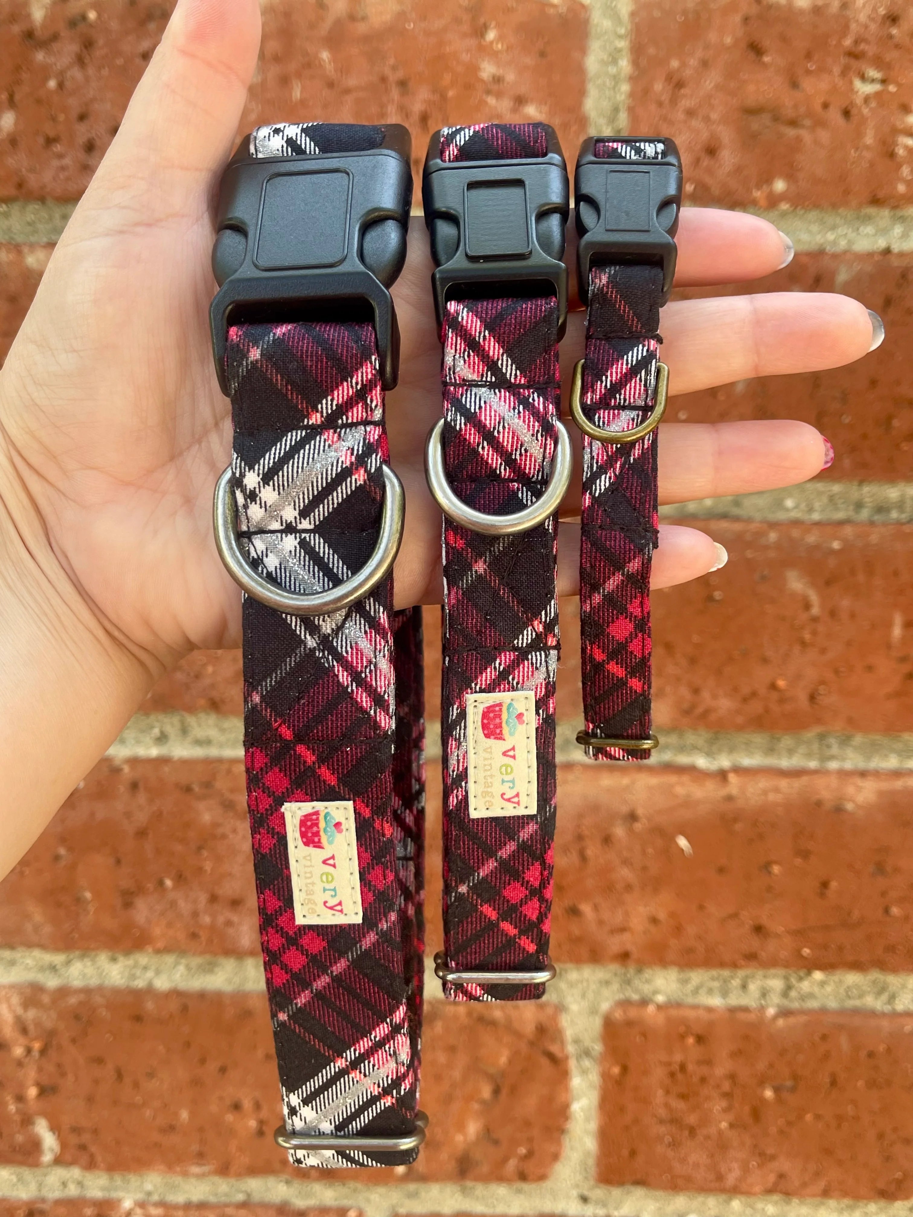 Three plaid dog collars held in a hand against a brick wall background