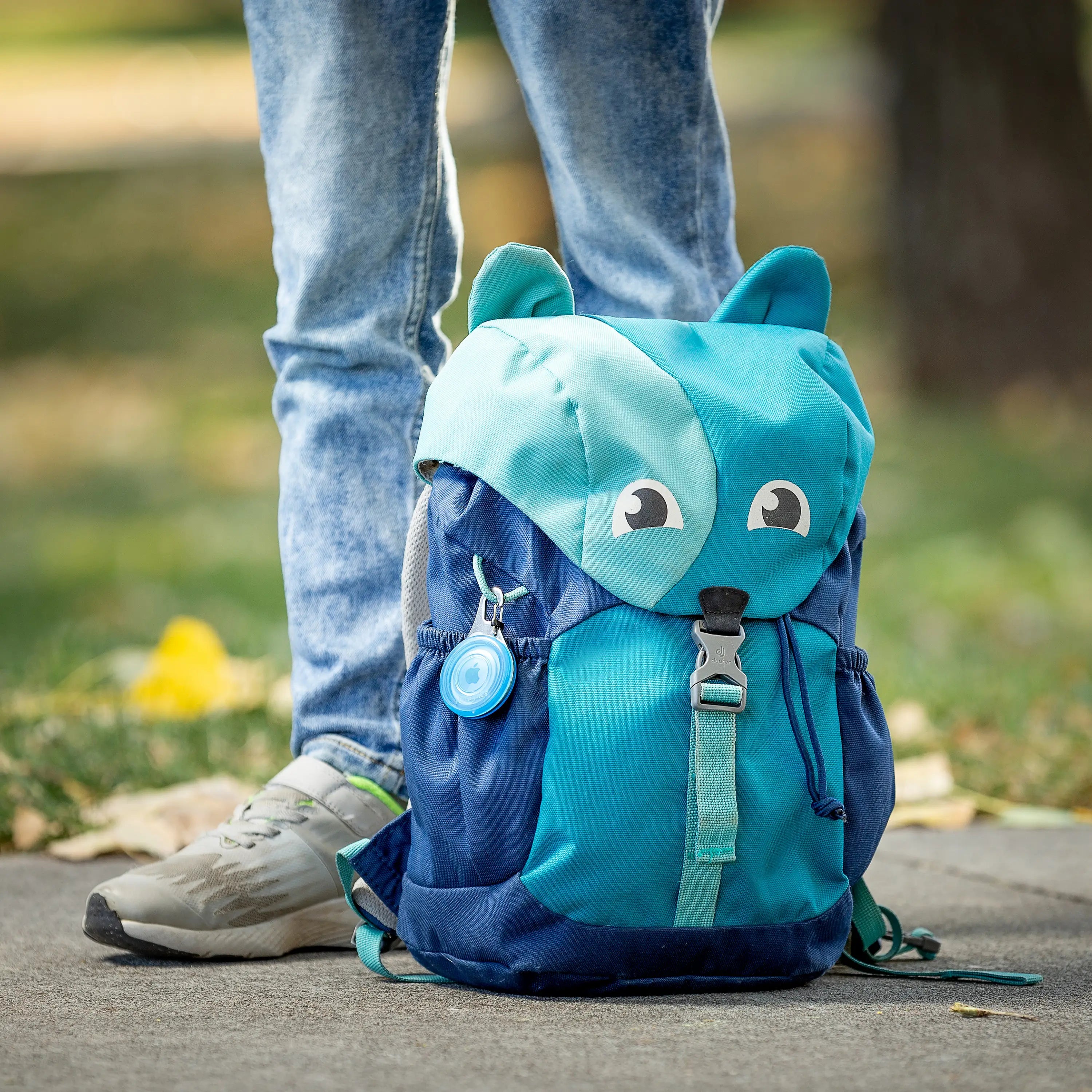 Blue children's backpack with animal ears and face on a person's back outdoors.