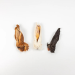 Three dried animal pelt or fur pieces arranged vertically on a plain white background, in brown, cream, and dark charcoal tones.