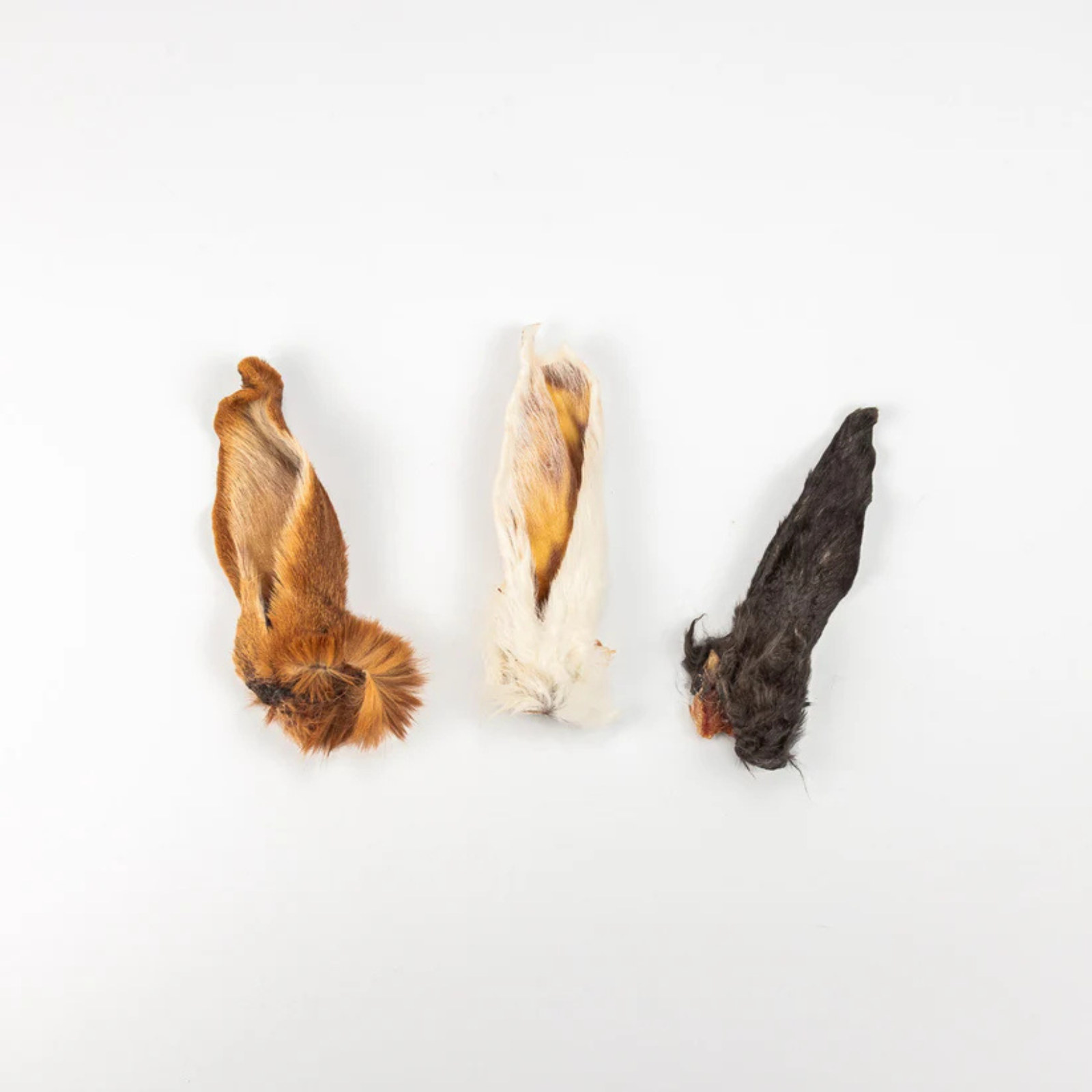 Three dried animal pelt or fur pieces arranged vertically on a plain white background, in brown, cream, and dark charcoal tones.
