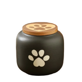 Black pet urn with paw prints on a wooden surface