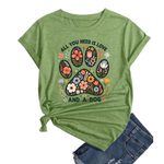 A green heathered short-sleeve t-shirt with a floral paw print graphic and the text 'ALL YOU NEED IS LOVE AND A DOG', styled flat-lay with blue jeans on a white background.