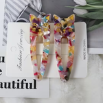 A pair of acrylic cat-ear hair clips with a colorful marbled pattern and gold cat face details, displayed on a white card
