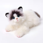 A fluffy faux-fur toy kitten lying down on a clean white background. The toy features a white body with black and gray patches on its face, ears, and tail, large blue eyes, and pink-tipped paws.
