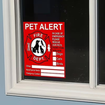 A red and white 'PET ALERT' window sign with a fire department-style emblem, shown attached to a dark window pane.