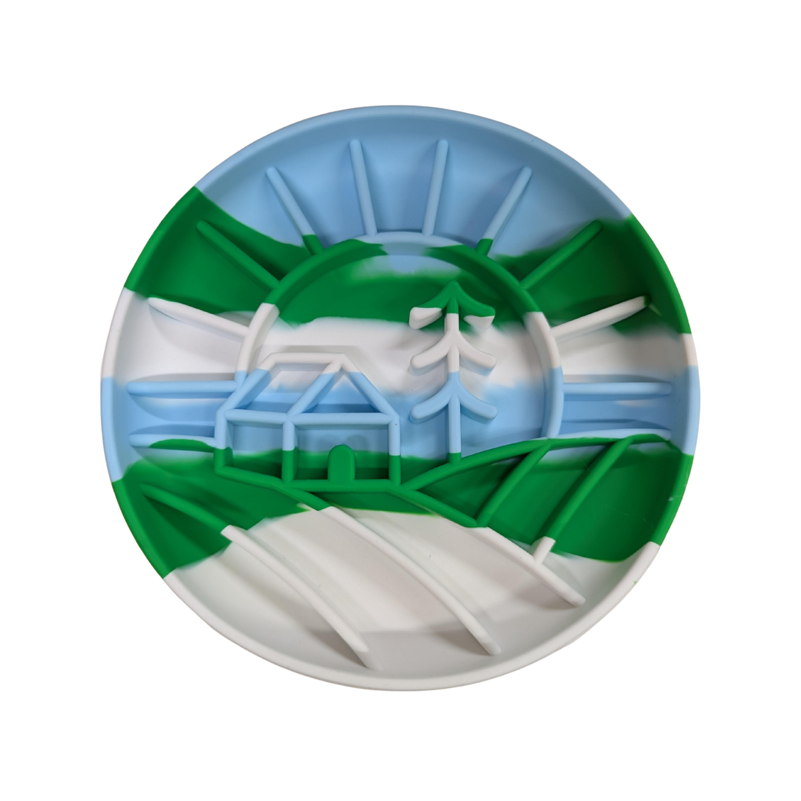 A circular silicone dog slow feeding bowl featuring a cabin, tree, and rising sun pattern. The bowl is light blue, green, and white.