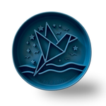 A round dark blue pet bowl with an embossed origami crane design over stylized waves and stars, with the brand name 'BARKS & BROWNIES' embossed at the bottom, shown on a white background with a soft shadow.