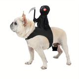 A light furred dog wearing a black Grim Reaper costume with a hooded figure holding a scythe and a red eye detail, photographed on a plain white background.