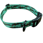 A green pet collar with a repeating pattern of black fish and small orange accents, featuring a black plastic quick-release buckle and a metal ring.