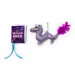 A purple glitter dragon plush toy with white wings and a bright purple feather tail, shown next to a small purple book titled 'The Dragon Rider' with a turquoise ribbon bookmark, on a plain white background.