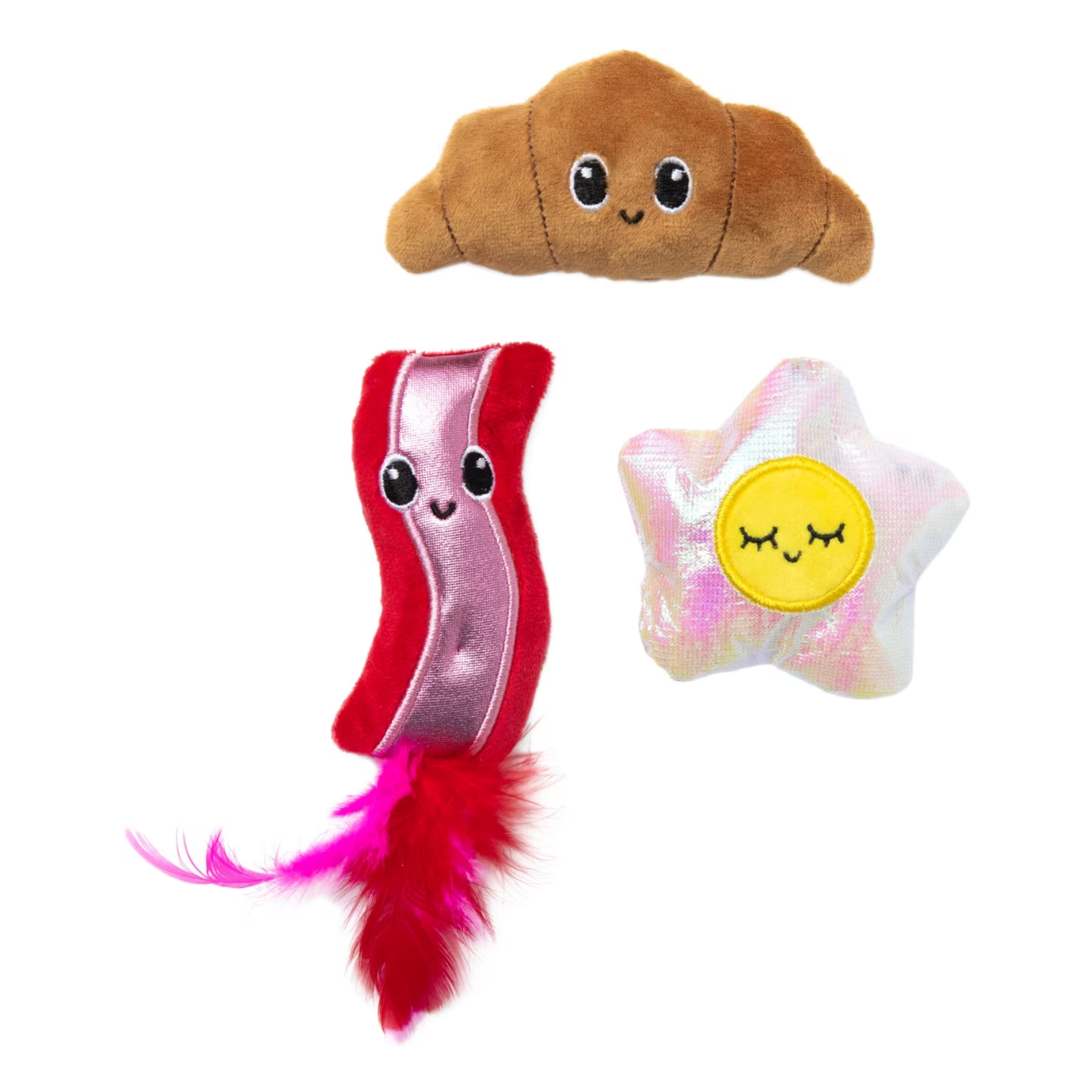 Three plush pet toys on a white background: a brown croissant-shaped toy with a face, a red-and-pink bacon-shaped toy with a feather tail, and a white iridescent star-shaped toy with a yellow smiling face.