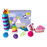 A party-themed cat toy set on a white background, featuring a purple and blue striped cylindrical toy with a feather topper, a colorful party hat, a white plush heart with red heart glasses, a pink donut-shaped toy, a green spring, a blue pom-pom, a purple ball, and a purple fluffy ball, arranged in front of a branded product box.