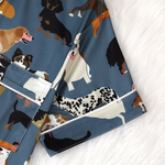 A close-up of a pair of shorts with a blue base and an all-over print of various dog illustrations, laid flat on a white textured surface.