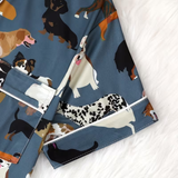 A close-up of a pair of shorts with a blue base and an all-over print of various dog illustrations, laid flat on a white textured surface.
