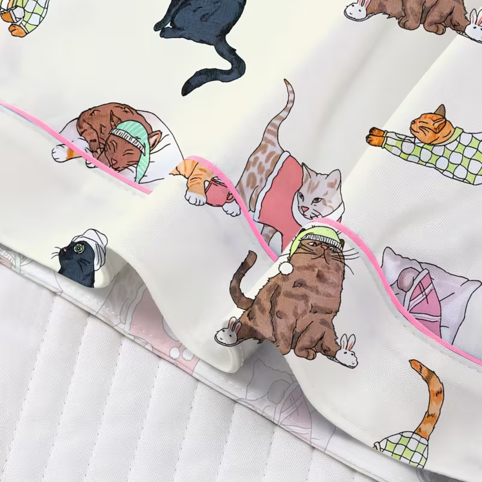 A close-up of a white pajama featuring a colorful cartoon cat print and a pink piping edge.